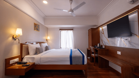 Close-up of the bed and a long wooden desk/console area with a television mounted above the mirror at Pravasa Stay, Vadodara.