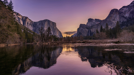 Dramatic sunset over Yosemite Valley with purple and yellow hues mirroring on the calm lake.