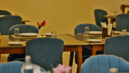 A detailed view of wooden dining tables paired with plush teal chairs and formal glassware - Tathastu Chavri Resort, Jawai