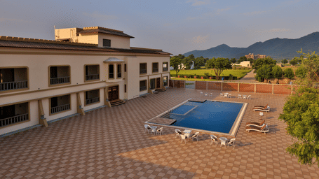 A high-angle shot of the spacious paved courtyard, the pool, and the distant mountain range - Tathastu Chavri Resort, Jawai