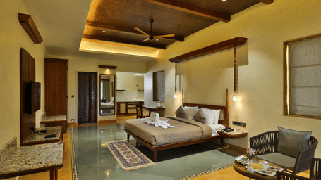 A wide-angle view of a deluxe bedroom featuring polished floors, a flat-screen TV, and a seating nook - Tathastu Chavri Resort, Jawai