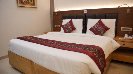 A neatly made bed in an Executive Room at The OnTime Hotel, Bangalore, featuring patterned pillows and a matching bed runner against a dark padded headboard flanked by wooden nightstands and reading lamps.
