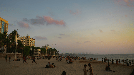 An overview of Juhu Beach with many people on the shoreline during twilight hour and skyscrapers in the distance. It is a must-visit place on your itinerary of things to do in Mumbai in summer.