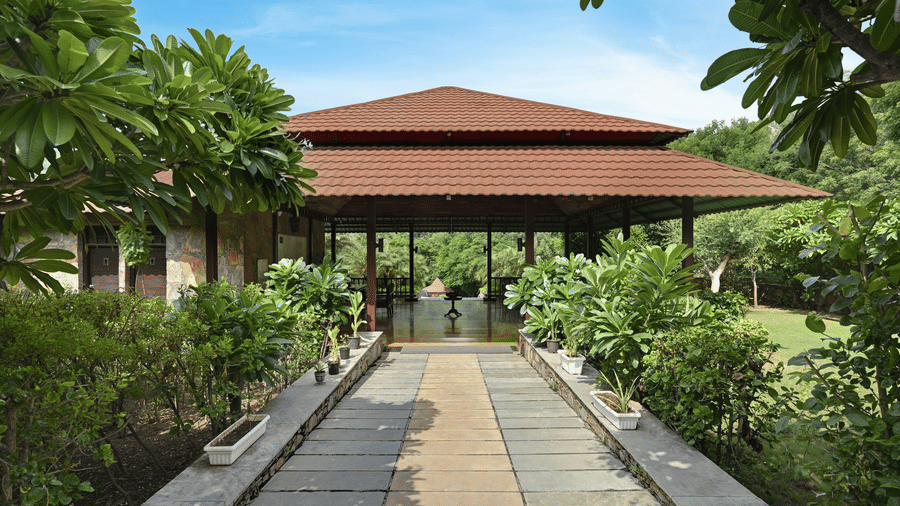 A symmetrical stone walkway leading towards a pavilion surrounded by trees and plants | Anandam Jungle Retreat Resort, Udaipur
