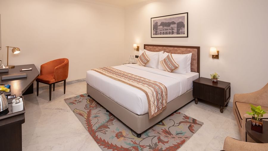 An image of a bedroom with bedside table, photo frame hanged on the wall, work desk with sofa chair, and a flat TV screen - Brij Eternity, Vrindavan