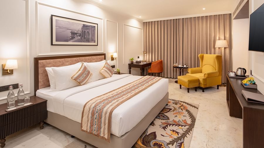An image of a bedroom with bedside table, photo frame hanged on the wall, work desk with sofa chair, and a flat TV screen - Brij Eternity, Vrindavan