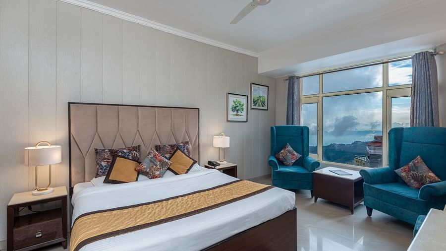 Shot on a well furnished room featuring a king size bed and a large window with two chairs placed near the window | DLS The Pearl