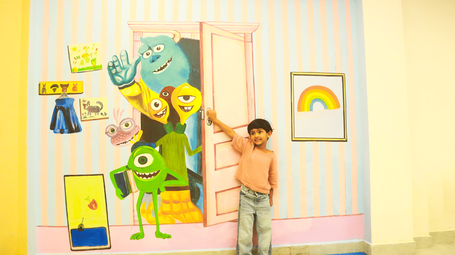 A young boy standing next to a colourful wall mural of animated monsters in the playroom at DNC Shevaroys Resort & Spa.