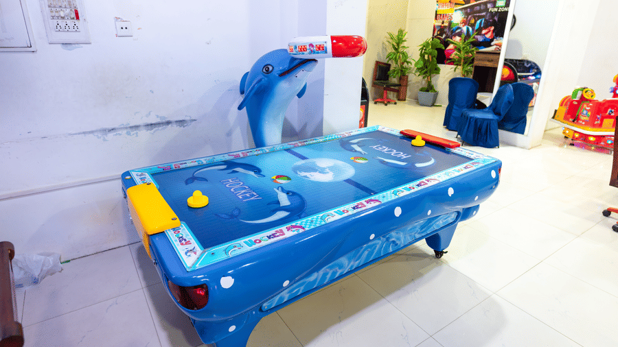 Dolphin-themed air hockey table at the DSF Fun Zone, DSF Grand Plaza, Tuticorin, with blue upholstered chairs and a virtual reality games poster in the background.