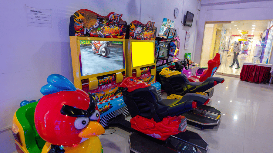 Arcade games at DSF Grand Plaza, Tuticorin with motorbike racing machines, a red bird-shaped ride, and a view through the doorway into the shopping mall corridor.
