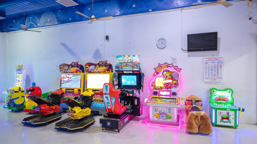 Wide view of the gaming arcade at DSF Grand Plaza, Tuticorin with racing simulator machines, cartoon character rides, a whack-a-mole game, and a claw machine under a star-painted ceiling.