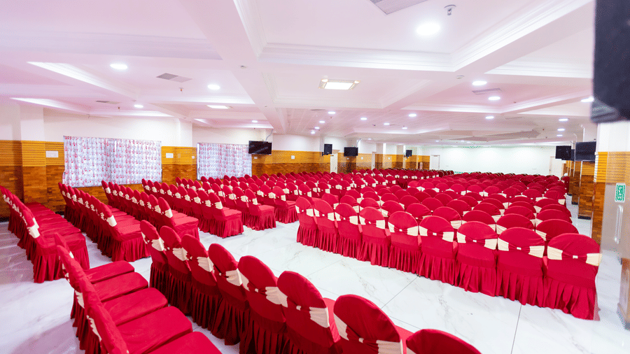 Irudhayam Hall at DSF Grand Plaza, Tuticorin arranged with rows of red chair covers tied with cream sashes, floral curtains, and wall-mounted screens.