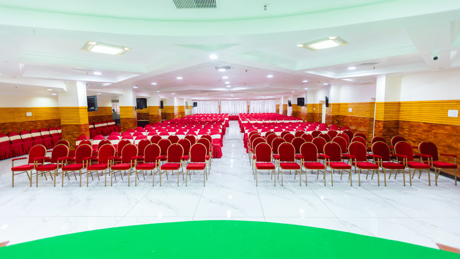 Irudhayam Hall at DSF Grand Plaza, Tuticorin set up theatre-style with rows of red chairs facing a green stage, wood-panelled walls, and a marble floor.
