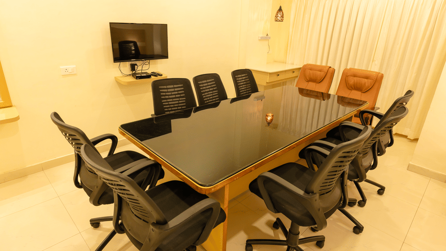 Boardroom at DSF Grand Plaza, Tuticorin with a glass-top table, black mesh chairs, 2 tan leather chairs at the head, and a wall-mounted television.