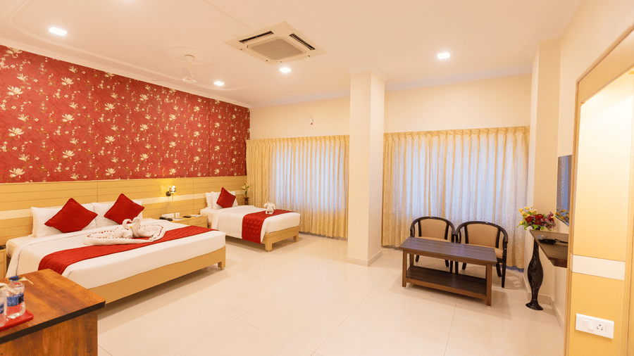 Club Room at DSF Grand Plaza, Tuticorin with a double bed and single bed, red floral wallpaper, red bed runners with a towel swan display, and a small seating area.