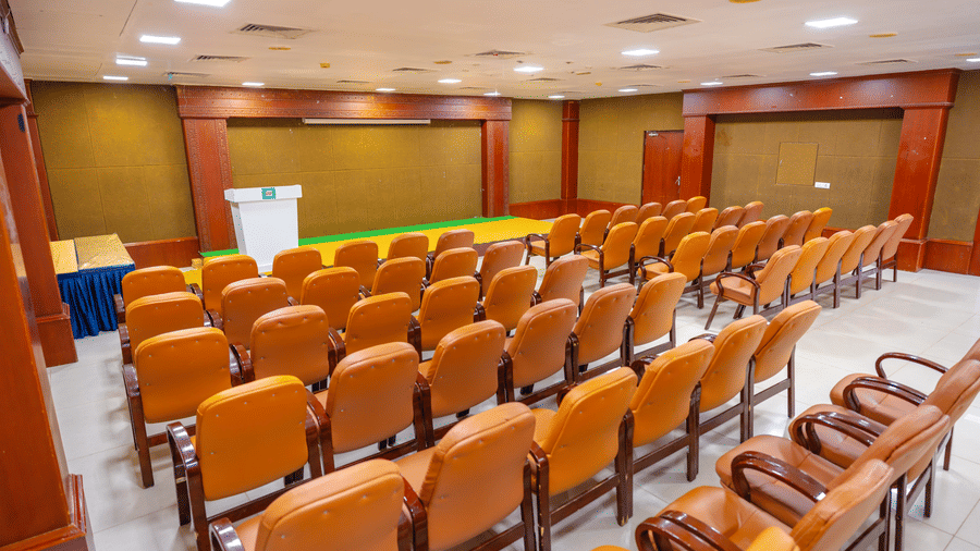 Conference hall at DSF Grand Plaza, Tuticorin with rows of orange chairs facing an empty stage with a lectern and a blue skirted table to one side.