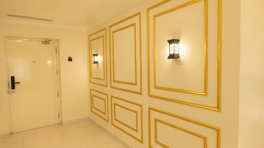 Suite entrance corridor at DSF Grand Plaza, Tuticorin with gold-framed decorative wall panels, wall sconces, and a room door with a keycard lock.