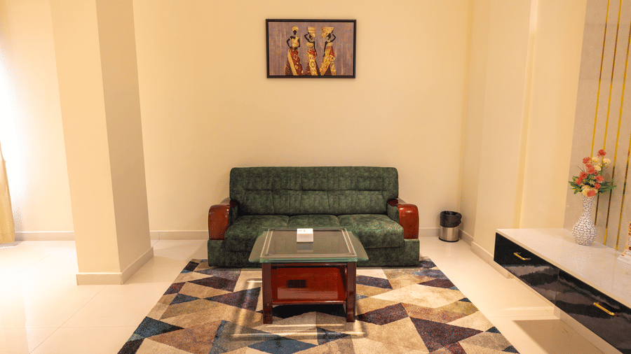 Suite living room at DSF Grand Plaza, Tuticorin with a green sofa, glass and wood coffee table, a colourful geometric rug, and framed African-motif art.