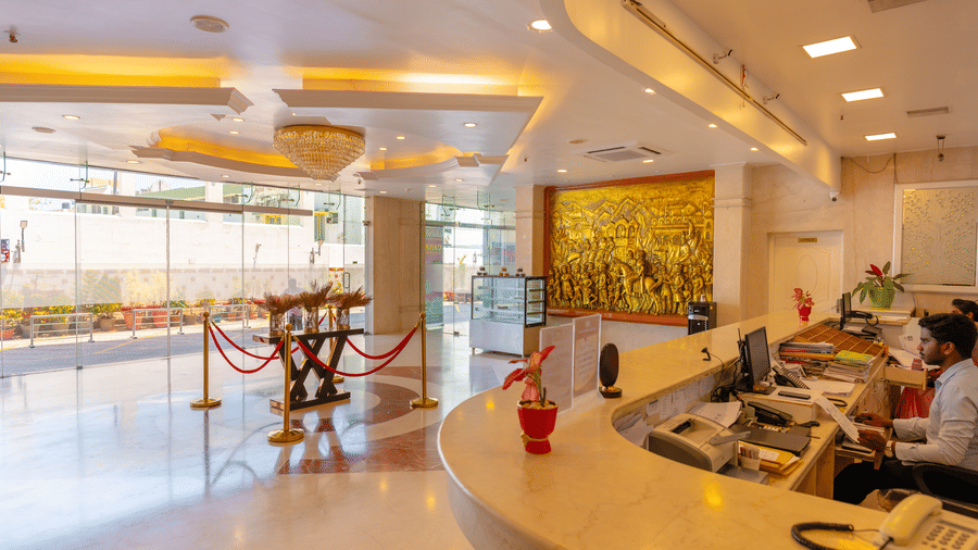 Lobby at DSF Grand Plaza, Tuticorin viewed from behind the reception counter, with a gold relief mural on the wall, glass entrance doors, and a crystal chandelier.