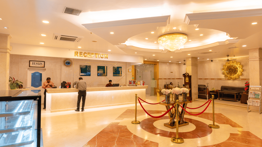 Lobby at DSF Grand Plaza, Tuticorin with guests at the reception desk, a crystal chandelier, a grandfather clock, and leather sofas by a gold sunburst decoration.