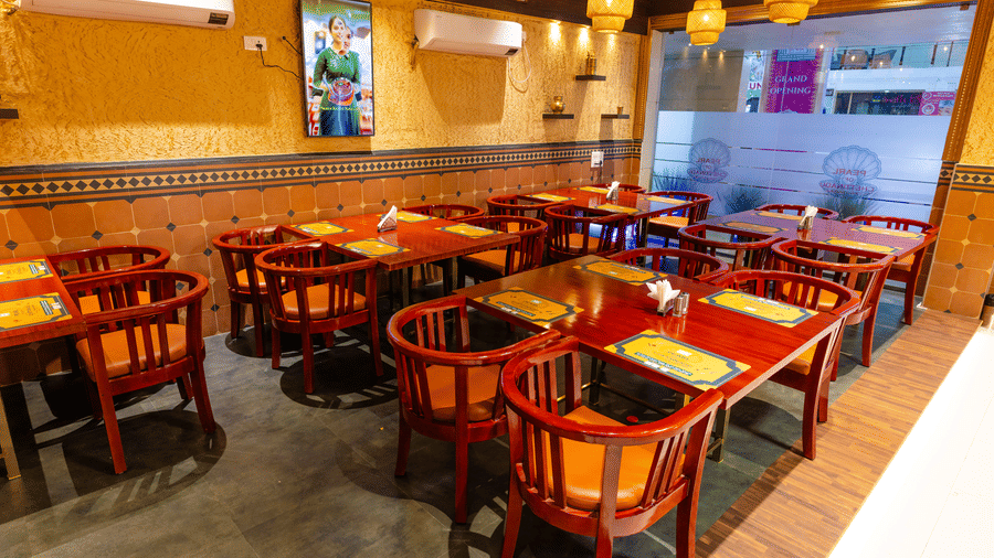 The Pearl of Chettinadu restaurant at DSF Grand Plaza, Tuticorin with woven pendant lamps, red chairs with orange cushions, and a wall-mounted screen.