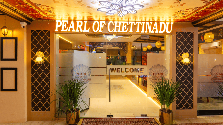 The entrance to Pearl of Chettinadu restaurant at DSF Grand Plaza, Tuticorin, with illuminated signage, glass doors, a welcome decal, and potted plants.