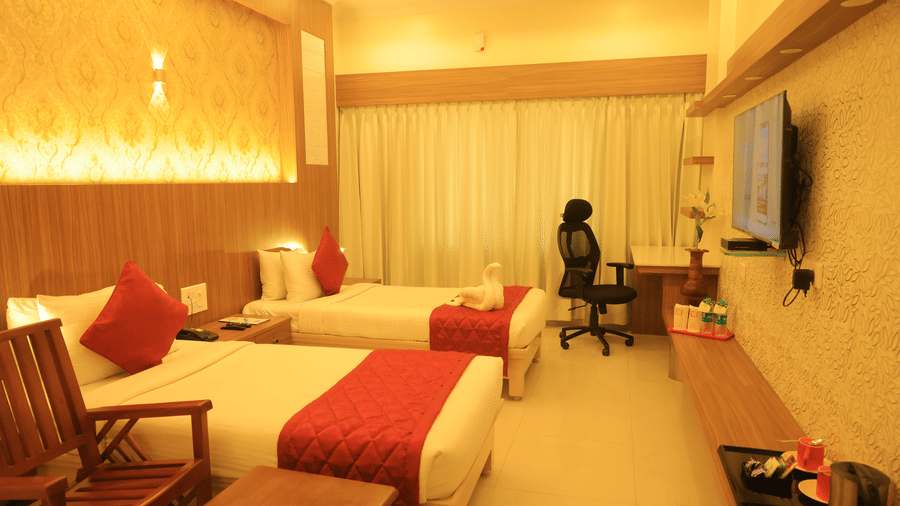 Royal Executive Room at DSF Grand Plaza, Tuticorin with 2 single beds with red runners, a gold damask headboard wallpaper, a wall-mounted TV, and a work desk.