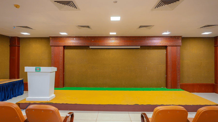 Empty stage at DSF Grand Plaza, Tuticorin with a lectern bearing the DSF logo, a yellow and green carpet, and orange chairs in the foreground.