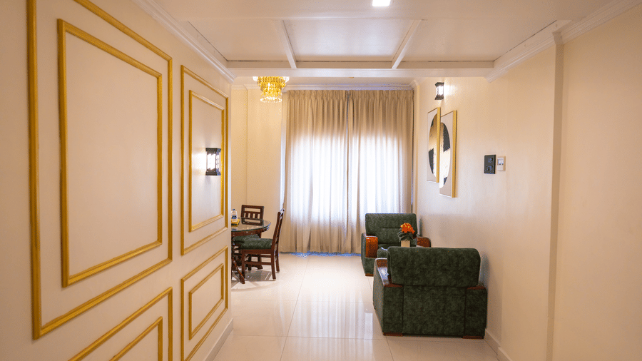 Suite entrance hallway at DSF Grand Plaza, Tuticorin with a gold-framed panel wall, coffered ceiling, chandelier, dining table, and green armchairs.