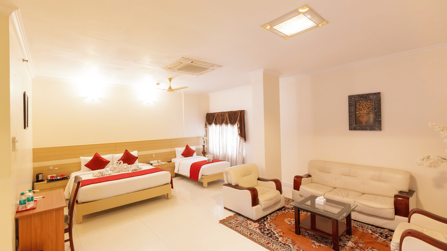 A Suite Room at DSF Grand Plaza, Tuticorin with a king bed and single bed in red and cream linens, plus a cream sofa seating area on a patterned rug.