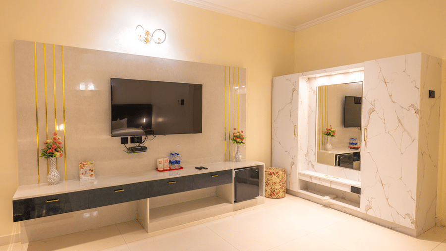 Guest room TV unit at DSF Grand Plaza, Tuticorin with a wall-mounted television, gold-striped panel, mini fridge, and a marble-effect wardrobe with mirror.