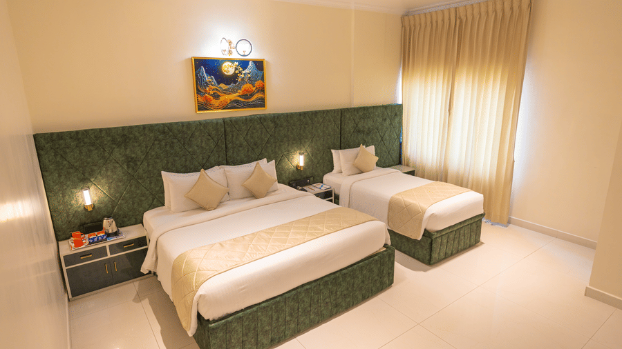Guest room at DSF Grand Plaza, Tuticorin with a double bed and single bed, green quilted headboard, framed landscape artwork, and a tea and coffee tray.