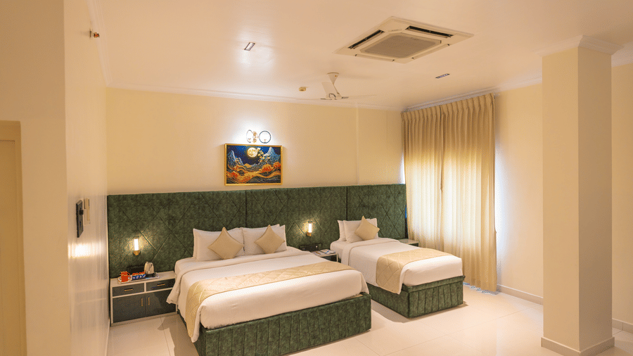 Guest room at DSF Grand Plaza, Tuticorin with a double bed and single bed, green headboards, floor-length curtains, and a cassette air conditioner above.