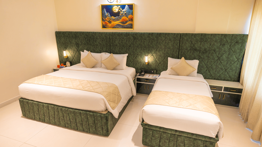 Guest room at DSF Grand Plaza, Tuticorin with a double bed and single bed side by side, green quilted headboards, and matching landscape artwork above.