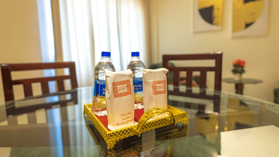 Welcome amenity tray at DSF Grand Plaza, Tuticorin with 2 DSF-branded paper sleeves over drinking glasses and 2 bottles of water on a gold ornate tray.