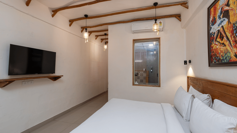 Bedroom with a king size bed, mounted television, ceiling beams, and painting, at Ewaka Ganga, Rishikesh.