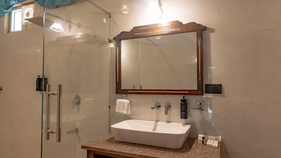 Bathroom vanity at Estherea Bagh, Ranthambore, featuring a wooden mirror frame, a sink, and a glass-enclosed shower area.