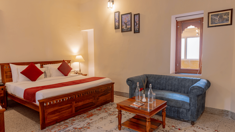 Bedroom at Estherea Bagh, Ranthambore, featuring a wooden bed, a sofa, and a small wooden coffee table.