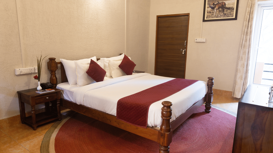 A bedroom interior at Estherea Bagh, Ranthambore, featuring a dark wood bed frame and a framed picture on the wall.