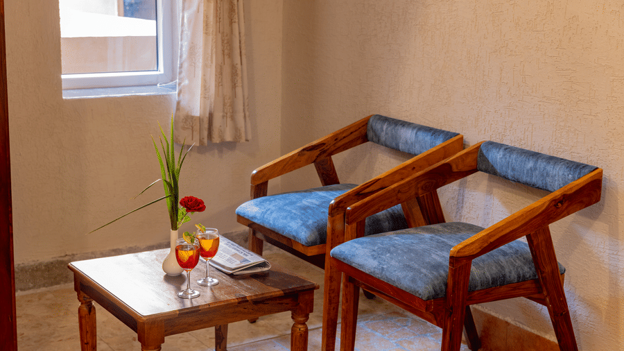 A close-up of 2 velvet armchairs and a wooden coffee table inside a guest room at Estherea Bagh, Ranthambore.