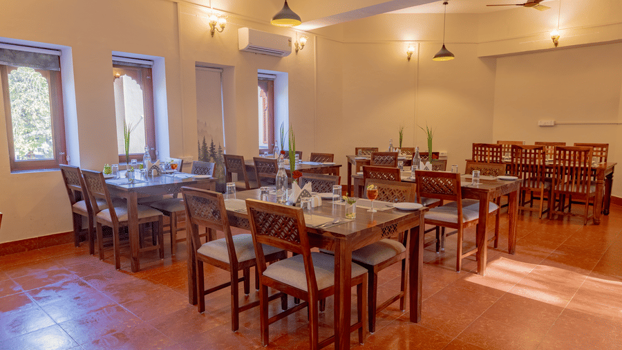 Multiple wooden dining sets arranged in the well-lit restaurant area at Estherea Bagh, Ranthambore.