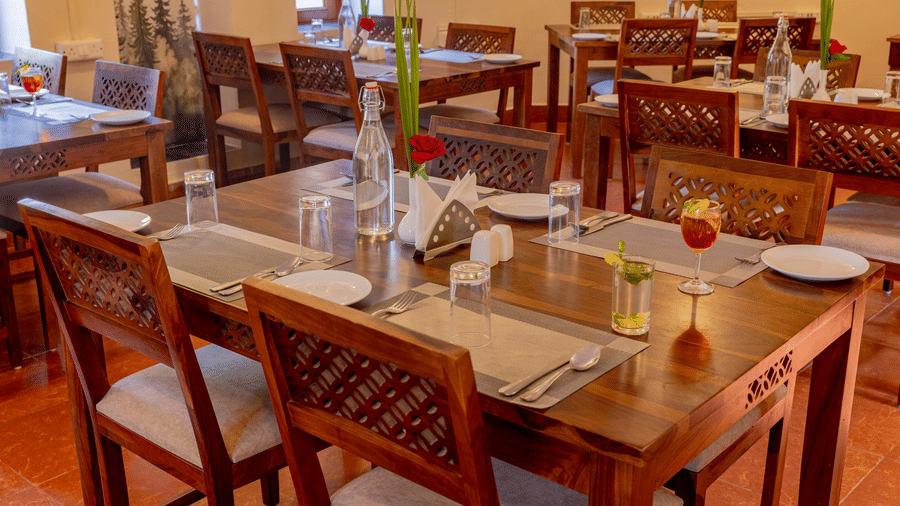 Close-up of an indoor dining table at Estherea Bagh, Ranthambore, set with water, glassware, and orange-colored drinks.