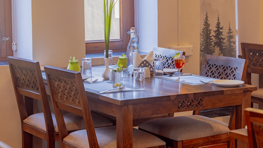 A wooden dining table at Estherea Bagh, Ranthambore, set for 4 people near a large window.
