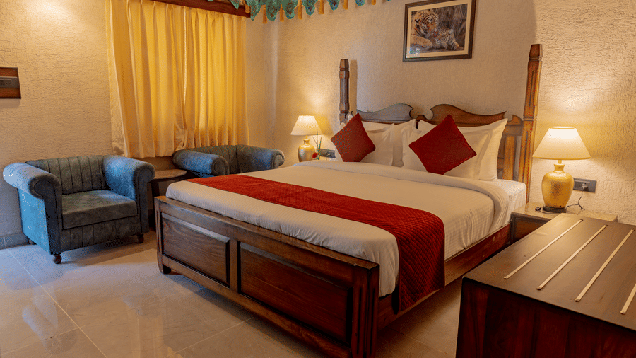 Interior bedroom at Estherea Bagh, Ranthambore, with a wooden bed, linens, pillows, armchairs, and decorative wall trim.