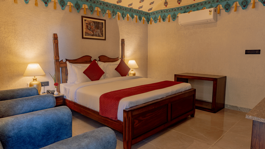 Guest room at Estherea Bagh, Ranthambore, showing a large bed with red accents, seating chairs, and a decorative border along the top of the walls.