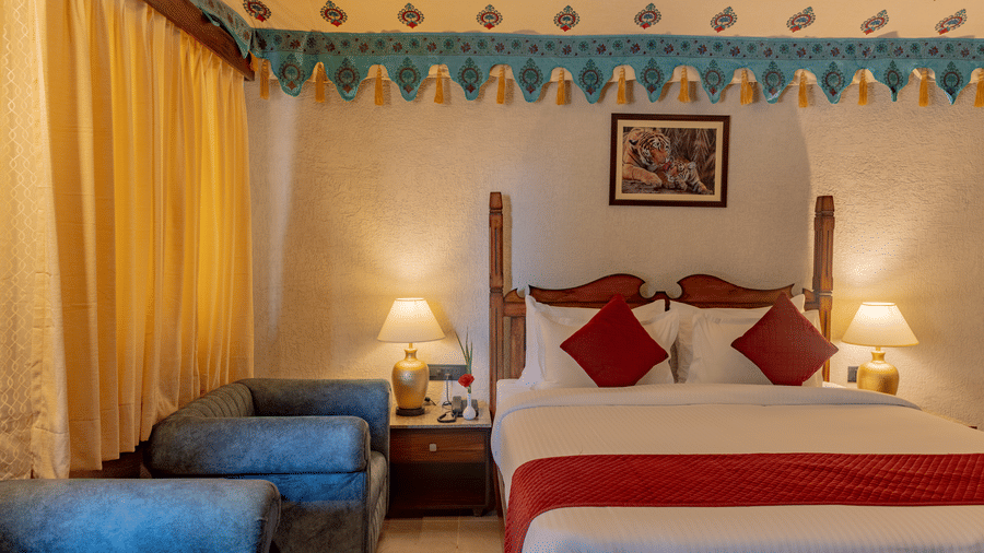 Bedroom interior at Estherea Bagh, Ranthambore, featuring a bed with red pillows, bedside lamps, and a decorative wall border.