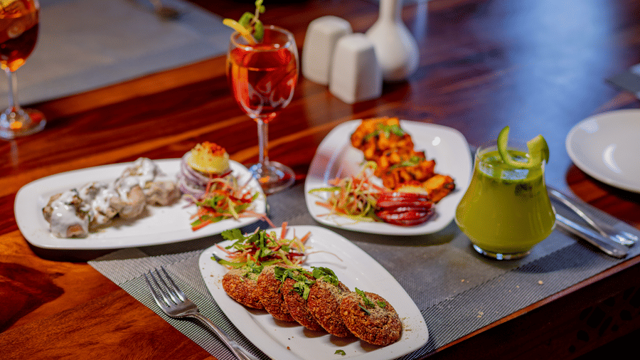 An assortment of 3 appetizer plates and colourful drinks on a wooden table at Estherea Bagh, Ranthambore.