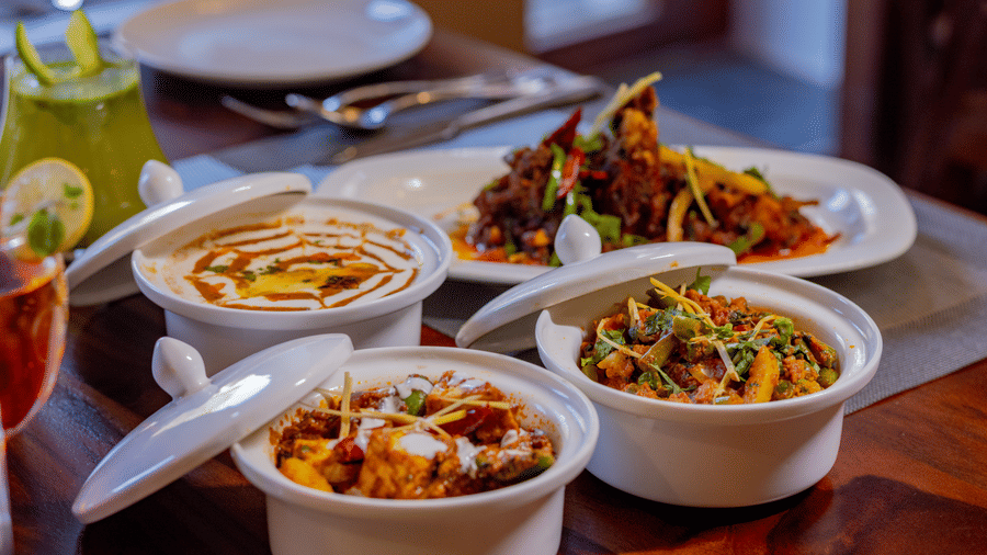 An assortment of Indian dishes in serving bowls placed on a wooden dining table at Estherea Bagh, Ranthambore.