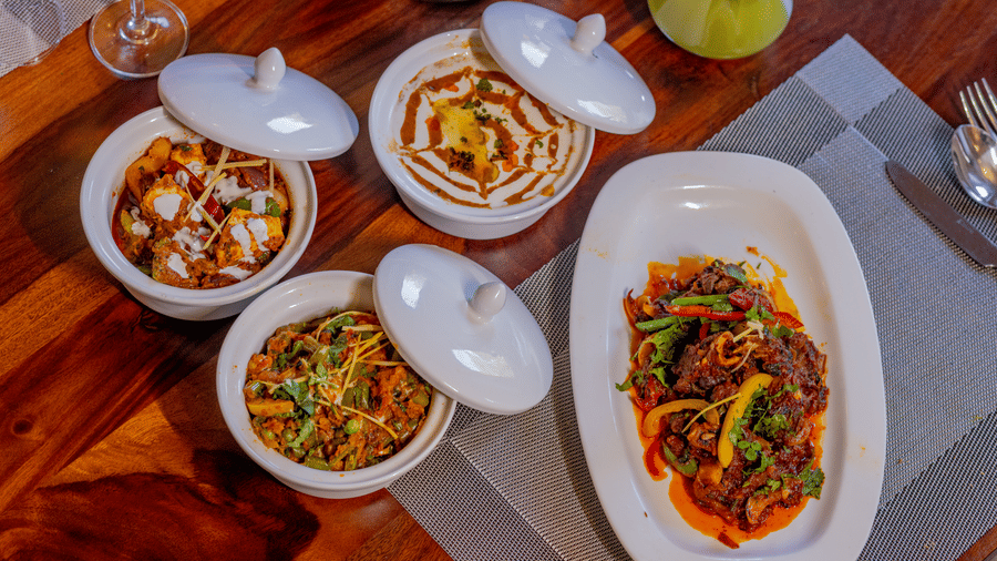 Overhead view of various Indian dishes and a stir-fry platter on a wooden table at Estherea Bagh, Ranthambore.