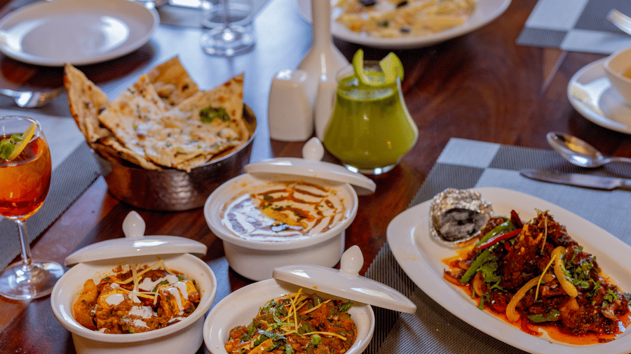 An overhead view of diverse Indian cuisine served in white bowls on a wooden table at Estherea Bagh, Ranthambore.
